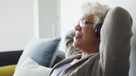 Afroamerikanische-ältere-Frau-Mit-Kopfhörern,-Die-Zu-Hause-Auf-Der-Couch-Musik-Hört