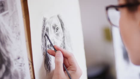 primer plano de un artista sentado en un caballete dibujando una imagen de un perro en carbón de una fotografía