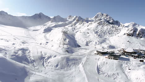 Christian-cross-on-the-side-of-the-hill-aerial-panoramic-shot-of-snowy-mountains-in-ski-resort-lighting-by-sun-pan-backwards--Kauntertal,-Austria