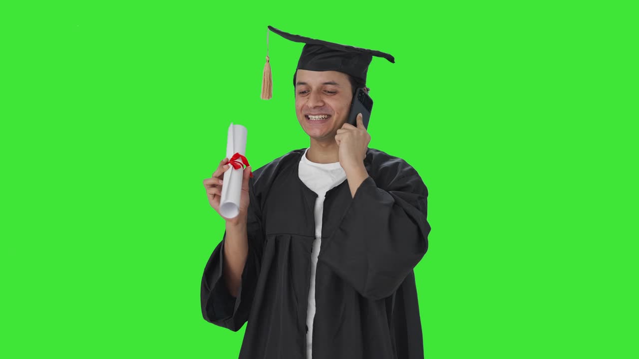Studente universitario indiano felice che parla al telefono dopo la laurea su schermo verde