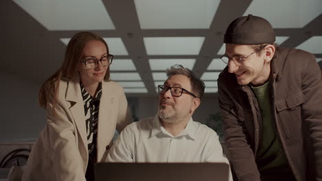 three colleagues collaborating around laptop, discussing project progress