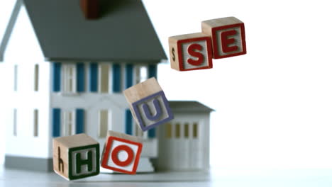 bloques de ortografía casa cayendo en frente de una casa en miniatura