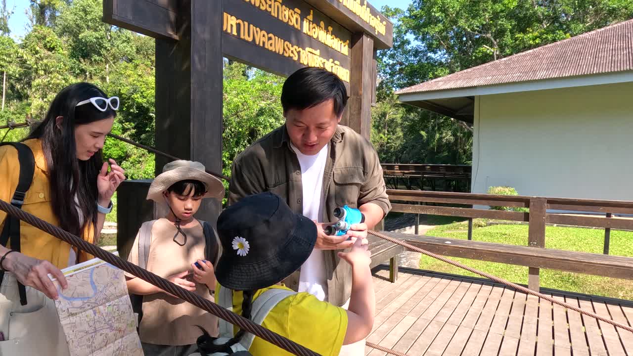 ครอบครัวชาวไทยศึกษาแผนที่และใช้กล้องส่องทางไกลขณะส ารวจสะพานในป่าเขตร้อน