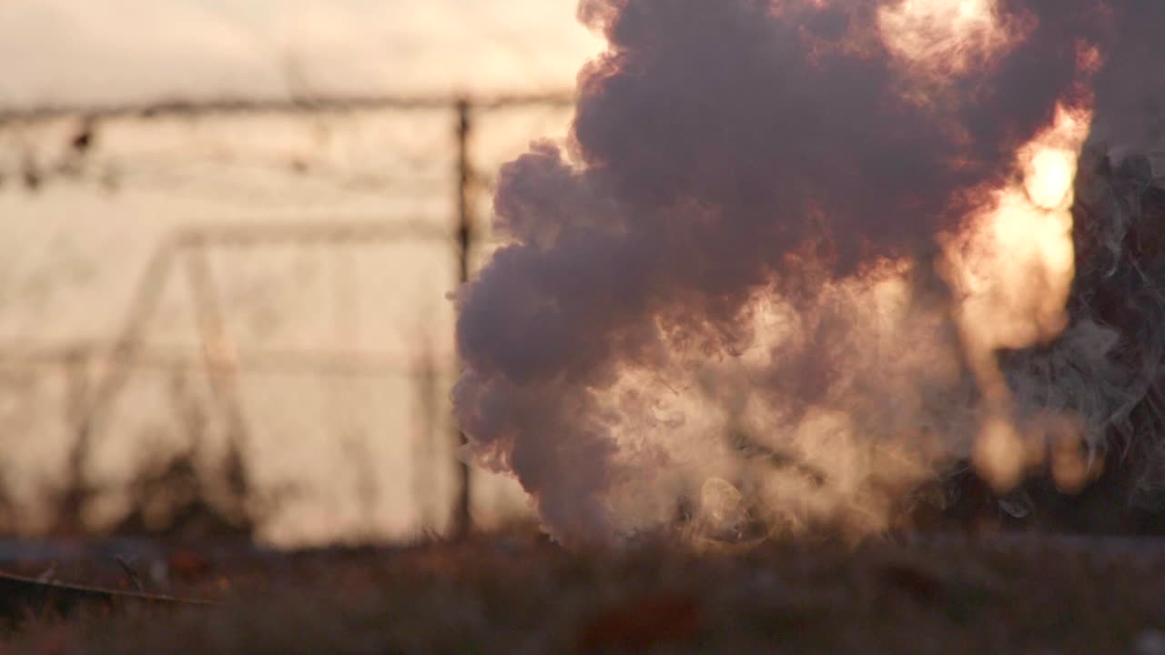 A smoke bomb at sunset is lit and is spraying smoke everywhere in slow-motion