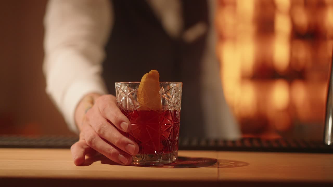 bartender manos sirviendo cóctel negroni con rodaja de naranja