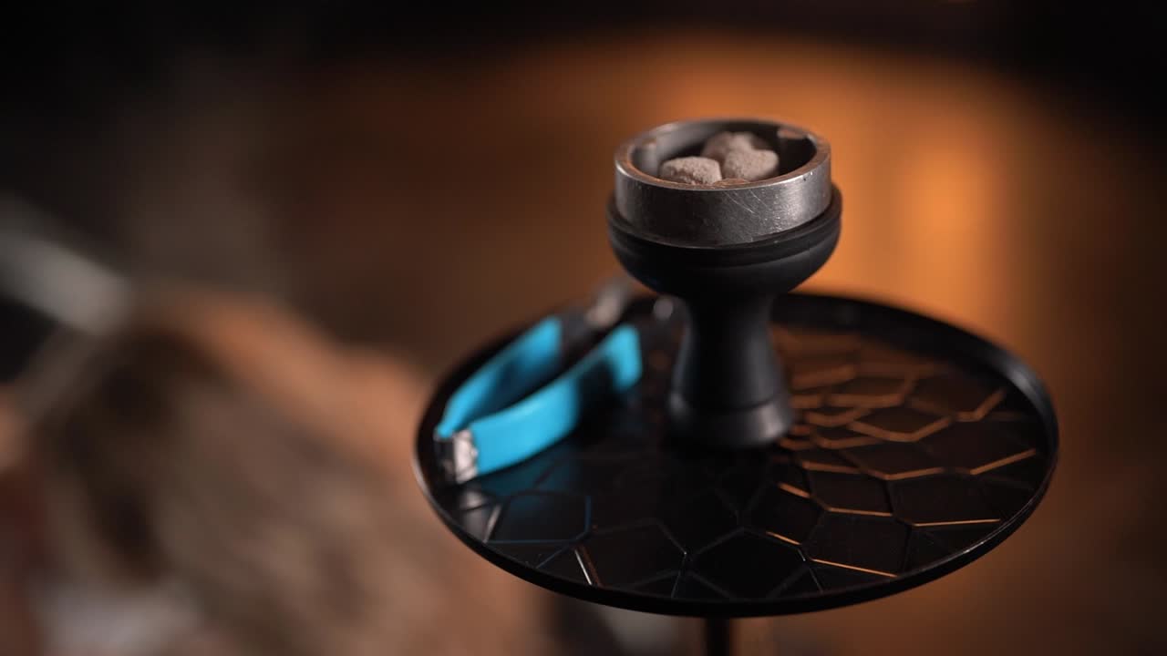 primer plano de un tazón de narguile con brasas sobre un fondo de mujer sexy y borrosa