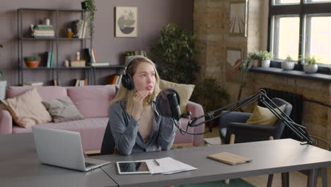 woman wearing headphones while talking into a microphone sitting at a desk with laptop, tablet and documents