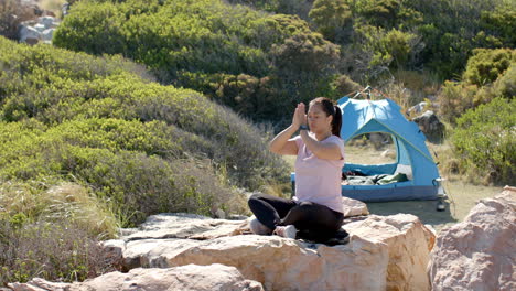meditating on rock, woman practicing yoga with tent in background during hike, copy space
