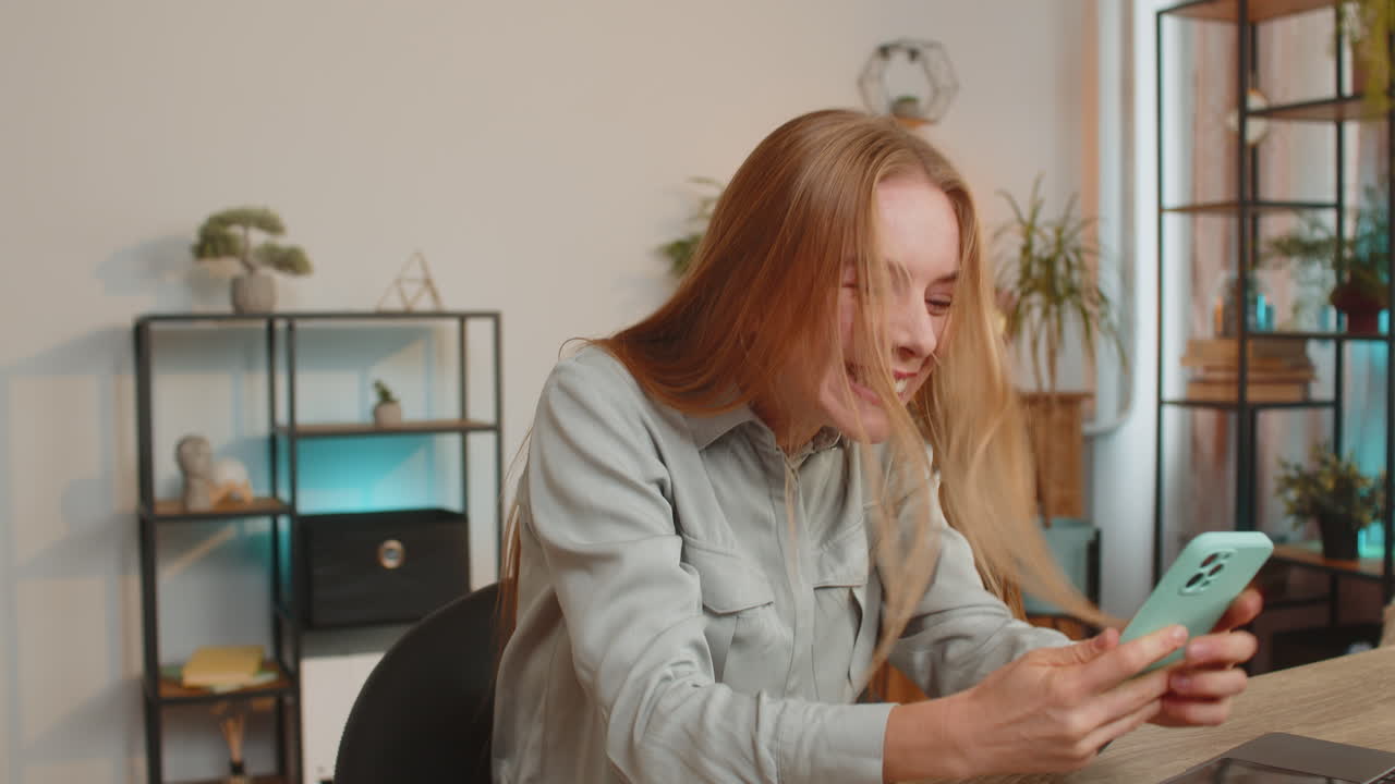 Happy mature woman freelancer using smartphone celebrating success victory winning lottery at table