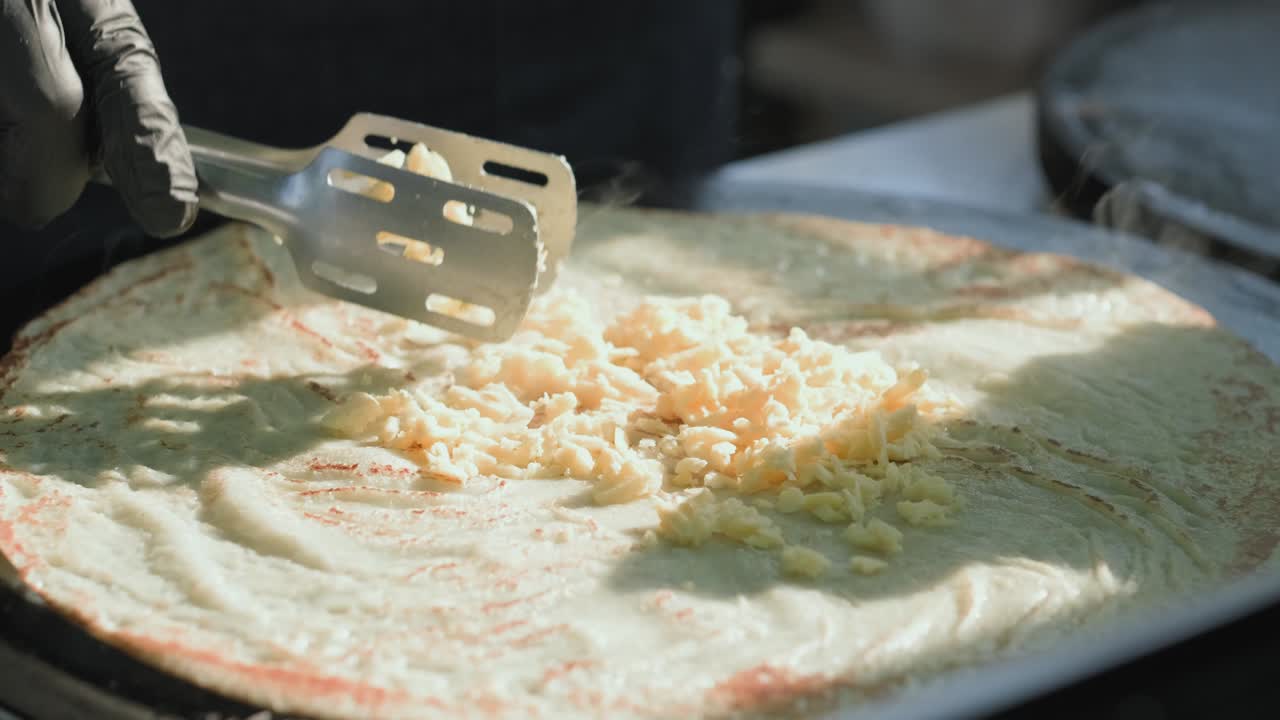 전문적인 프라이팬에서 러시아 팬케이크를 조리하는 측면 뷰: 요리사는 반죽을 팬에 부어 버리고 구운 팬케이크로 버섯과 치즈를 감싸고 있습니다.