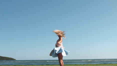 Gorgeous-blonde-holding-straw-hat-spinning-on-beach