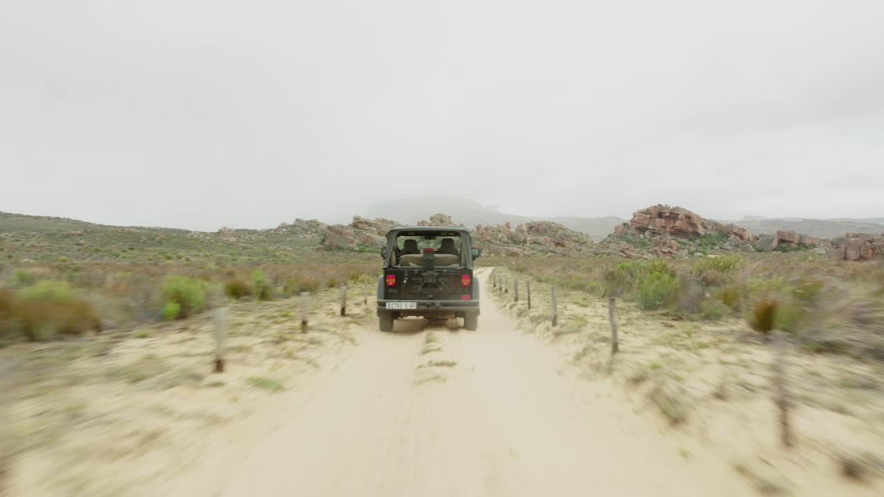 드론은 사막 풍경 위에 검은색 오프로드 차량 뒤에서 땅 위로 빠르게 날아가고 남아프리카 공화국의 세더버그 야생 지역의 바위 형성을 통해 날아갑니다.
