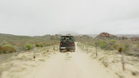 drone flies fast over the ground behind a black off-road vehicle over desert landscape and through rock formations in the cederberg wilderness area in south africa