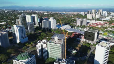 Aerial-pullback-of-a-modern-building-construction-site-and-yellow-crane-within-the-Southeast-Asian-cityscape-of-Las-Piñas,-Philippines