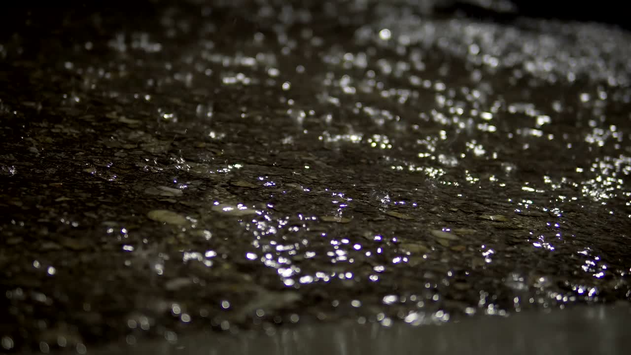 Rain falling on pavement asphalt surface at night, background loop