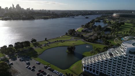 Aerial-establishing-shot-of-luxury-hotel,-Swan-River,-Matagarup-Bridge-and-skyline-silhouette-in-Perth-City-during-golden-sunset,-Western-Australia---cinematic-drone-flyover