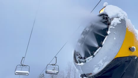 4k snow cannon producing snow at ski resort with cableway stopped in background. ski resort, snowmaking, winter holiday concept.