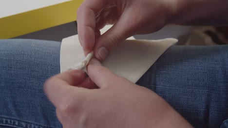 holding fabric over their thigh a seamster crimps and pins preparing the square fabric to be made into a face mask in response to the coronavirus pandemic