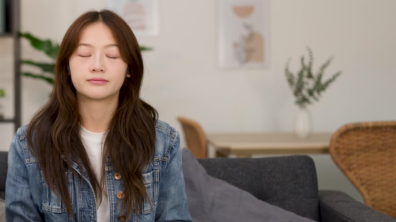 Young woman on couch shrugs with uncertain expression in bright indoor living room setting