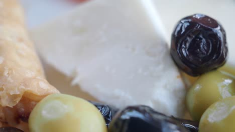 close-up of olives, feta cheese, and other food items on a white plate