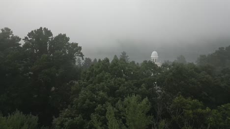 Foggy-forest-aerial-reveals-stately-old-hotel-on-shore-of-misty-lake