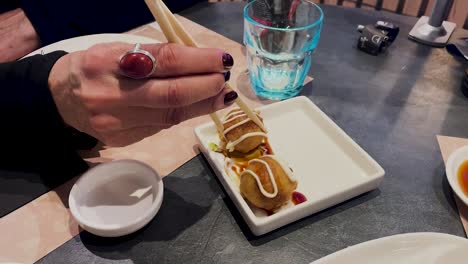 We-see-female-hands-with-chopsticks-taking-some-battered-octopus-balls,-and-soaking-them-in-some-sauces