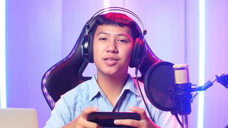 Ragazzo asiatico che tiene in mano lo smartphone e parla alla telecamera durante una diretta streaming.