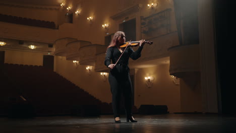 lonely young female violinist is playing fiddle in music hall full-length portrait of musician