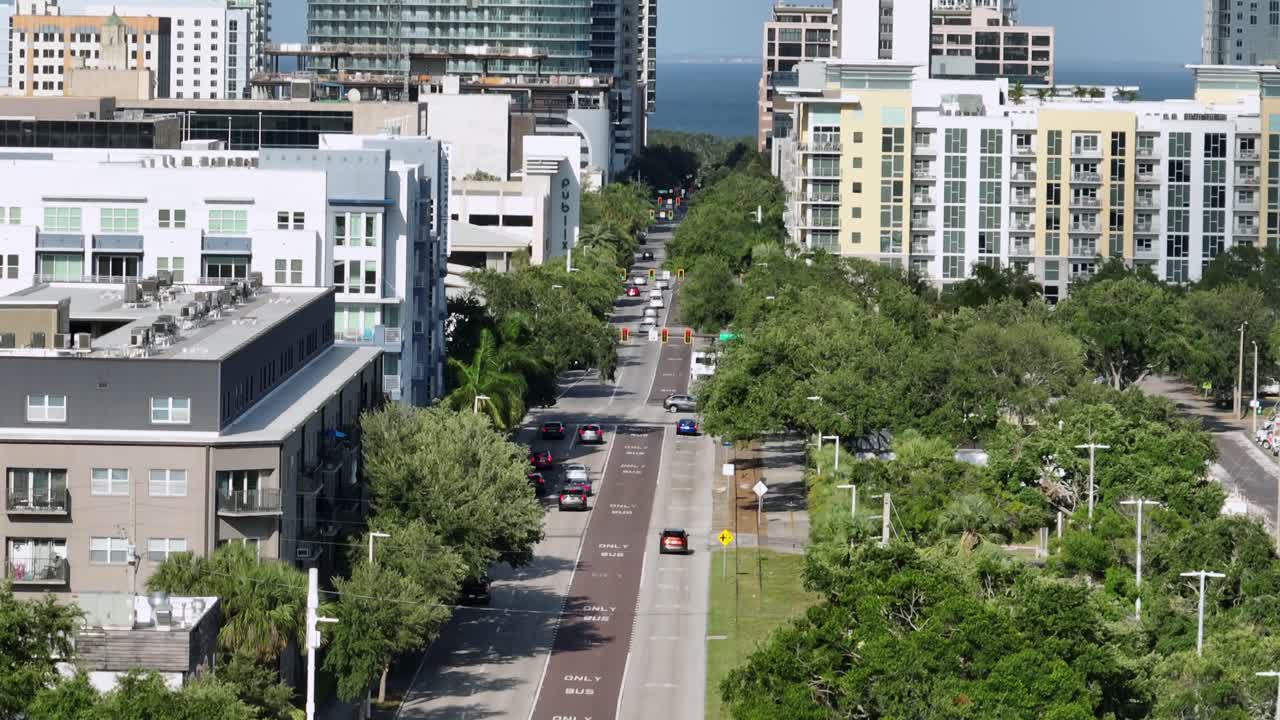 Downtown St. Petersburg, Florida, with towering modern buildings and lush tree-lined streets. Urban landscape is complemented by a glimpse of the waterfront in background under a clear blue sky.FL,USA