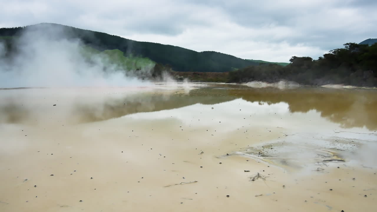 Hydrothermal area with boiling yellow colored water of lake green mountains in background - Wai-o-Tapu, New zealand
