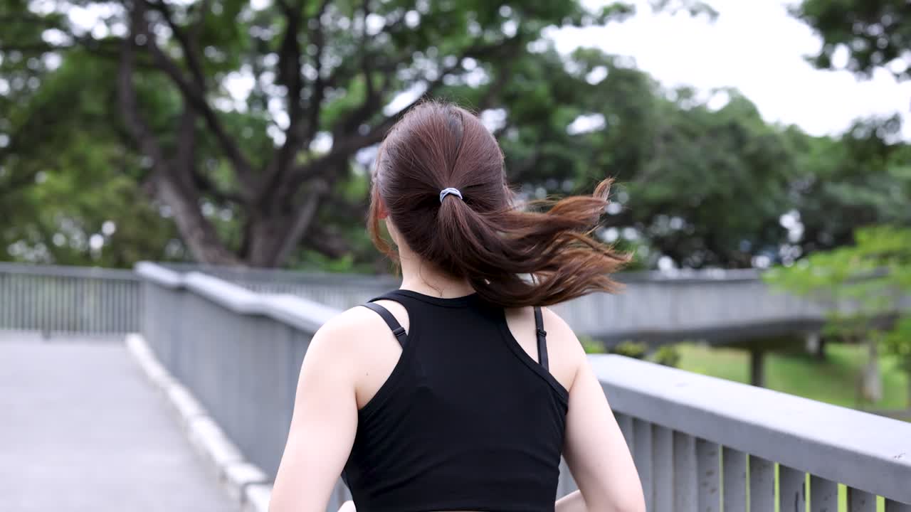 晴れた日、公園の小道をジョギングする女性の後ろ姿