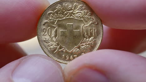 macro shot of male finger holding swiss golden twenty franc coin with helvetia and swiss cross