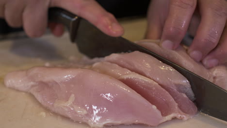 cerca de manos femeninas cortando carne de pollo cruda con un cuchillo sobre una tabla de cortar