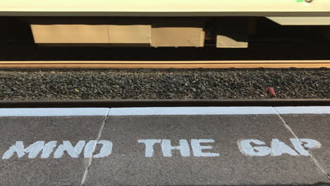 uk october 2018 - wheels on a train roll along a track past white stencilled writing on a grey concrete platform that says, “mind the gap”