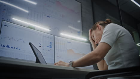 sad female stock exchange trader monitoring real-time stocks on multi-monitor computer and digital tablet in office at night, soaking financial loss. investment agent stressed about bad economy news.