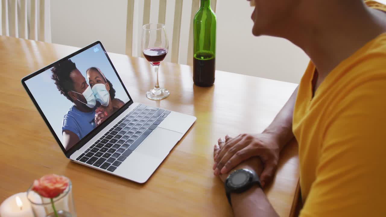 Mid section of african american man with wine while having a video call on laptop at home