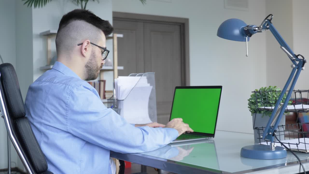 sobre el hombro de un joven empresario que trabaja desde la oficina en una computadora portátil con pantalla verde