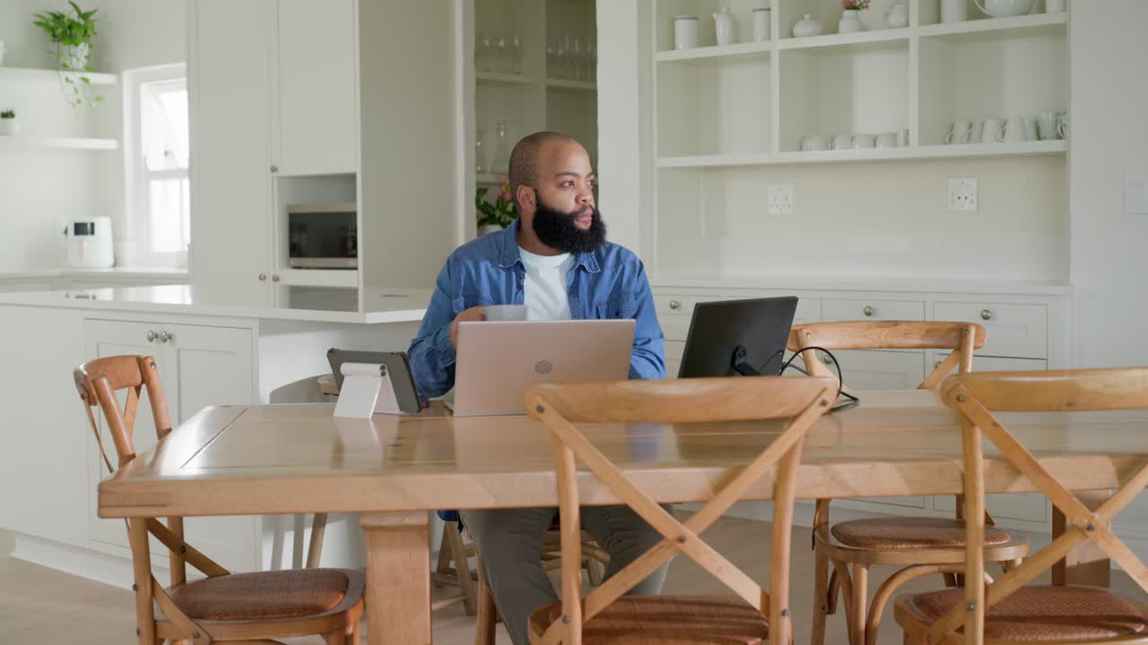 African American man sitting at home table, typing on laptops, answering phone after alert for work