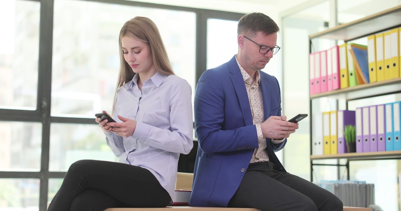 Businesswoman and businessman sit in office focusing on phones