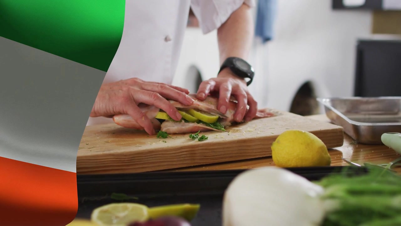 Chef che aggiunge erbe nella cavità del pesce, premendo e strofinando spezie, mostrando un tagliere con sovrapposizione di bandiera per cucinare.