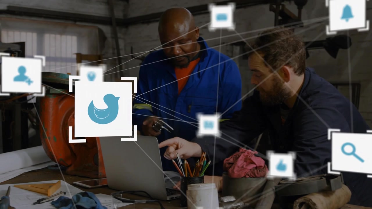 Technician tapping laptop and colleague leaning generating social icons mapping workshop workflow