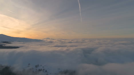 aerial,drone shot, over a clouds, in front of snowy forrest, mountain peaks and sunset colors