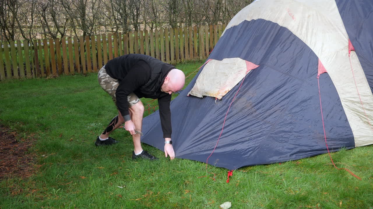 A bald man taking down a tent removing pegs