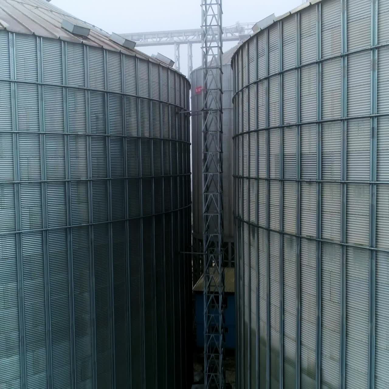 Massive tanks of elevator storage factory. Metal exterior of huge granary complexes on foggy day. Support between the containers