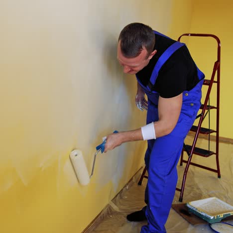 man painting walls of room. young male decorator painting wall in the empty room
