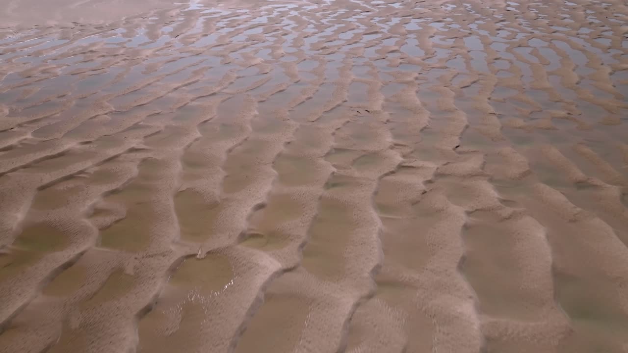Flying over rippled sands and clear seawater pools on a sunny day. Fleetwood, Lancashire, UK.