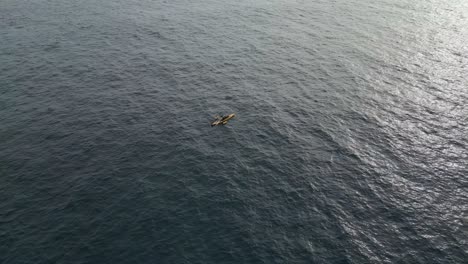 Toma-De-órbita-Aérea-De-Un-Solo-Kayak-Sobre-El-Océano-Con-El-Sol-Reflejando-El-Agua-Del-Océano