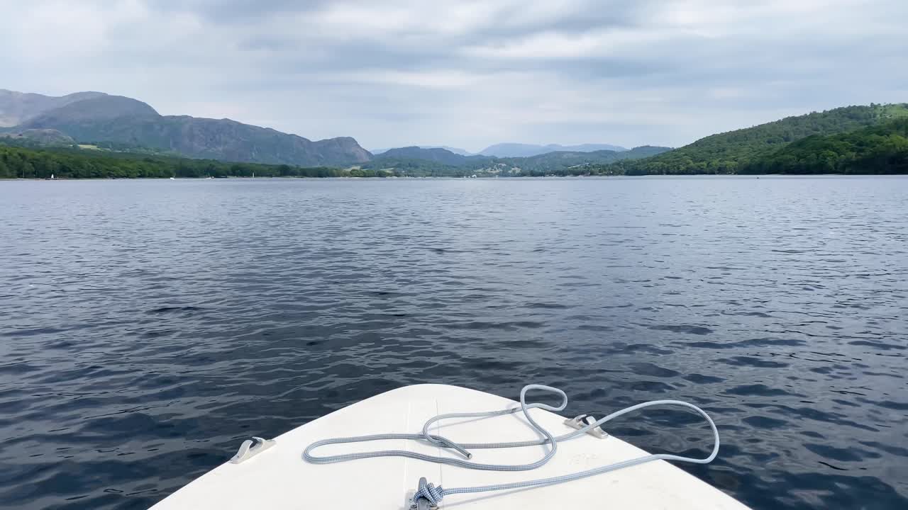una vista panorámica hacia adelante de la proa de un pequeño barco a motor blanco que conduce a lo largo del agua de coniston en el distrito de los lagos, reino unido