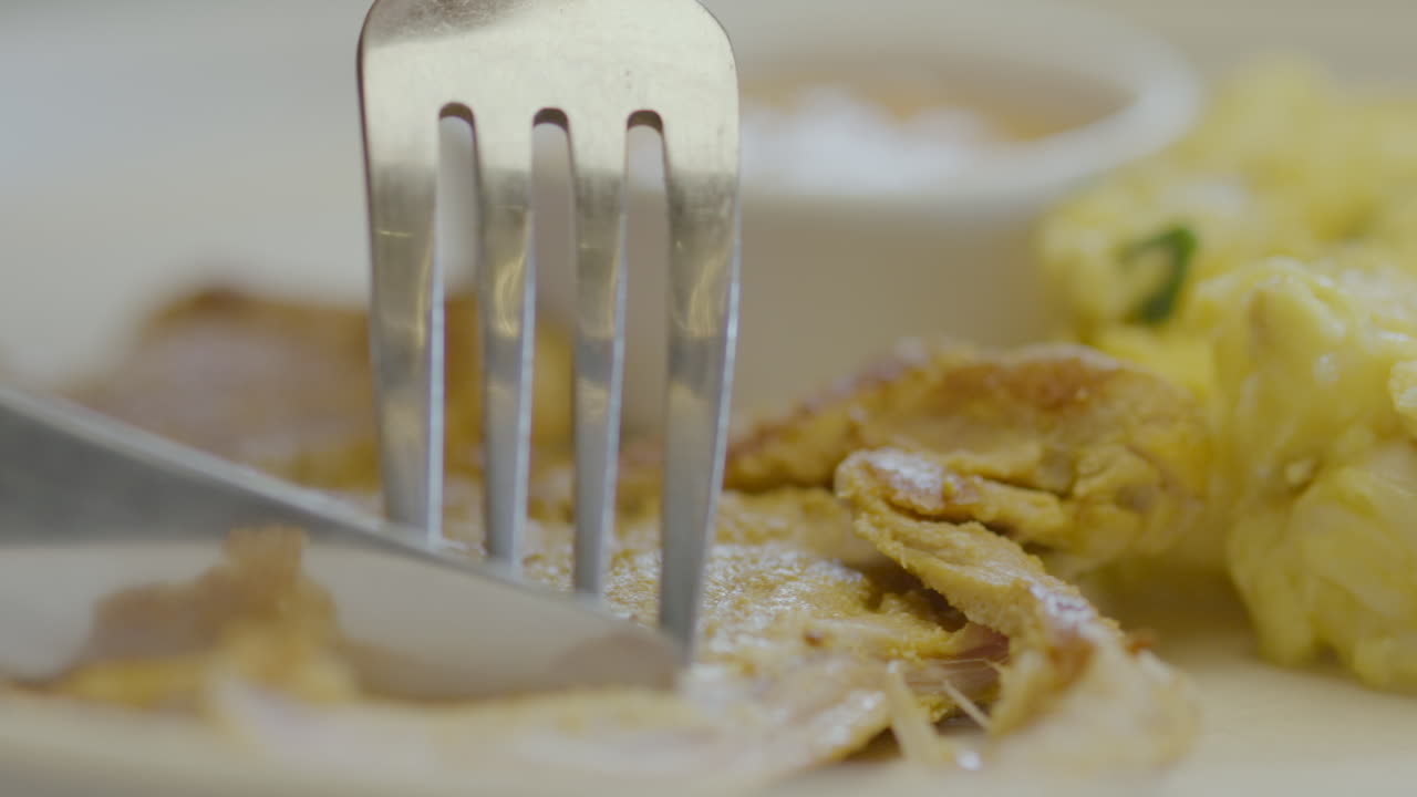 Close-up of a fork and knife cutting tender meat accompanied by mote pillo and sauce