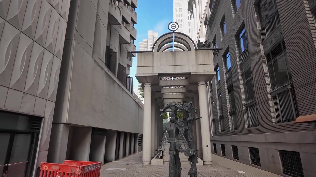 Un metraje de gran angular revela un impresionante corredor arquitectónico en el Embarcadero de San Francisco, con columnas geométricas, una escultura de arte contemporáneo, líneas nítidas y luz brillante del día.